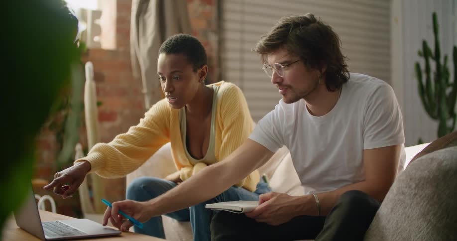 A man and woman sit at home looking at a laptop