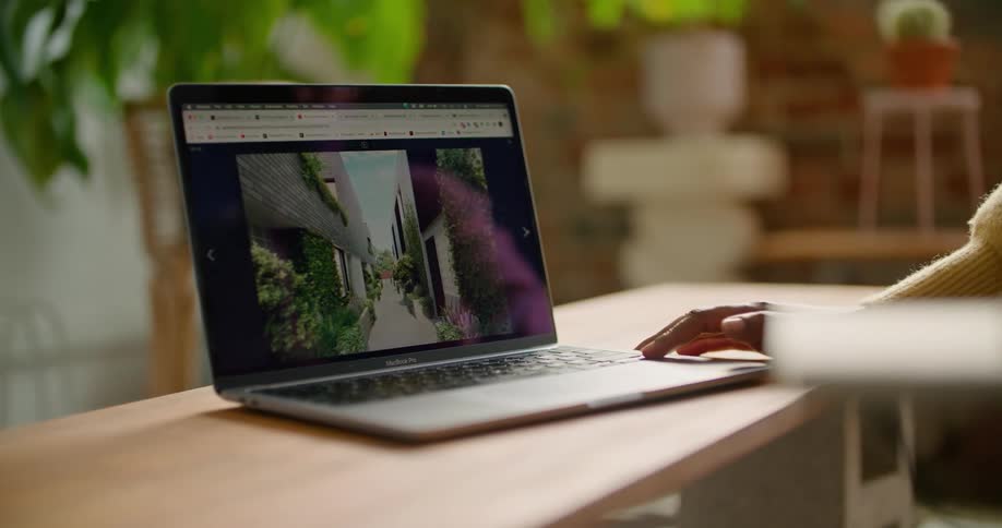 A person in a room sitting by a desk and using a laptop with a wall in the background