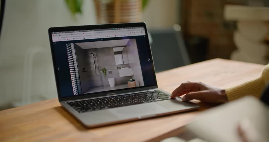 A person in a room sitting by a desk and using a laptop with a wall in the background