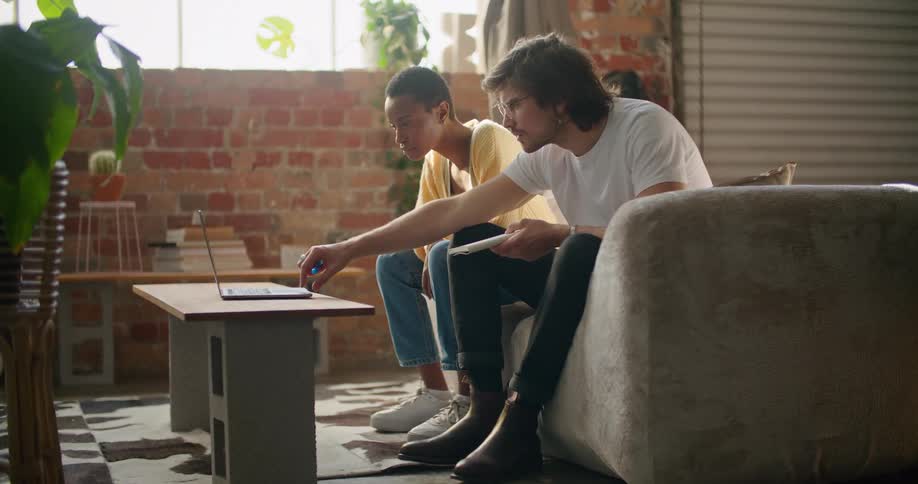 A man and woman squint and lean forward to look at a laptop sitting on a table made of cement blocks