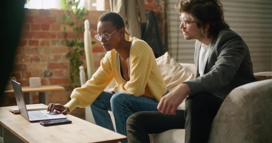 A man and woman are sitting on a couch together and looking at a laptop