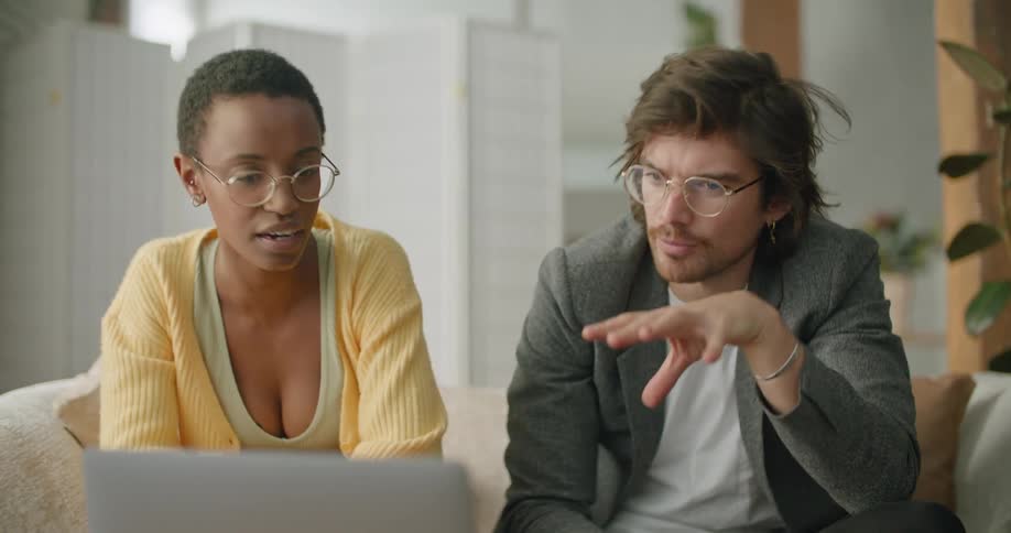 A man and woman talk while viewing a laptop
