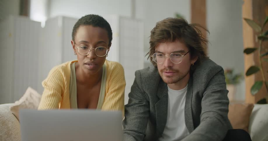 A man and a woman sitting on a couch in a living room with a laptop computer nodding in agreement as the man reaches forward and starts typing
