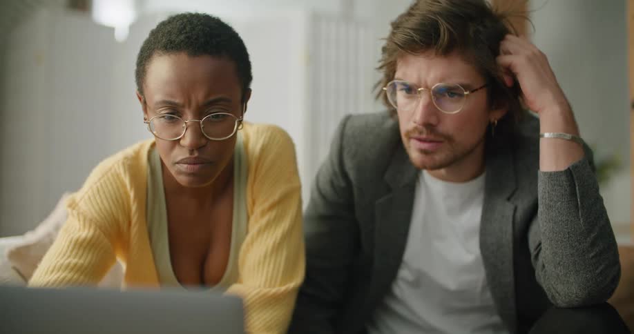 A man and woman are sitting indoors and looking at a laptop