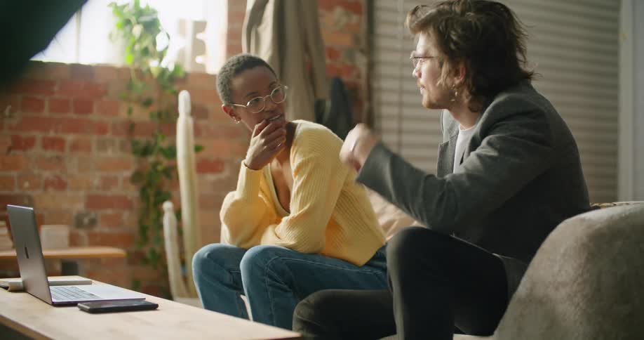 A woman types on her laptop while seated on the couch with a friend