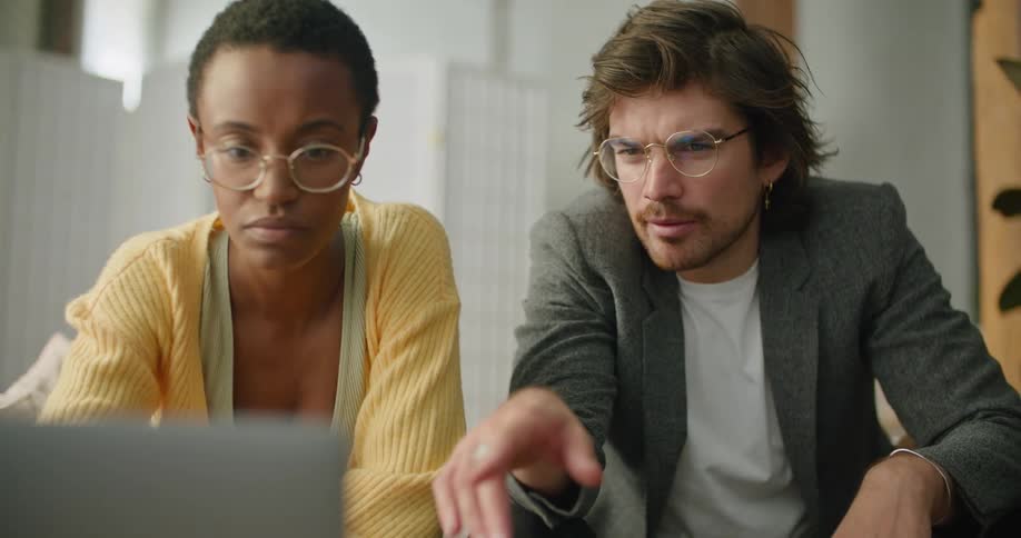 A man leans forward and types on a laptop after talking with his female coworker sitting beside him