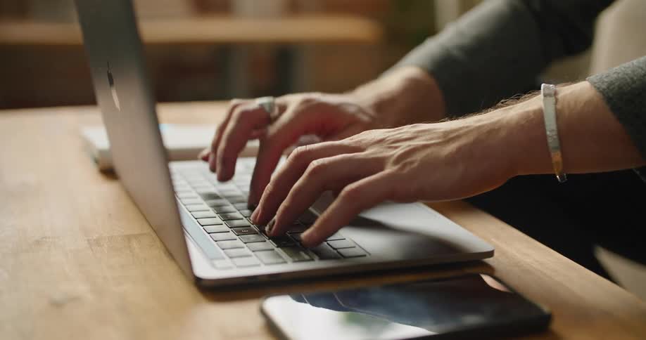 A man writes a note in a notebook then types on a laptop on a coffee table