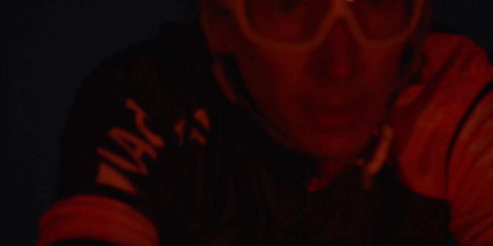 A man in bike helmet with white glasses is riding a bike with a red light shining in his face