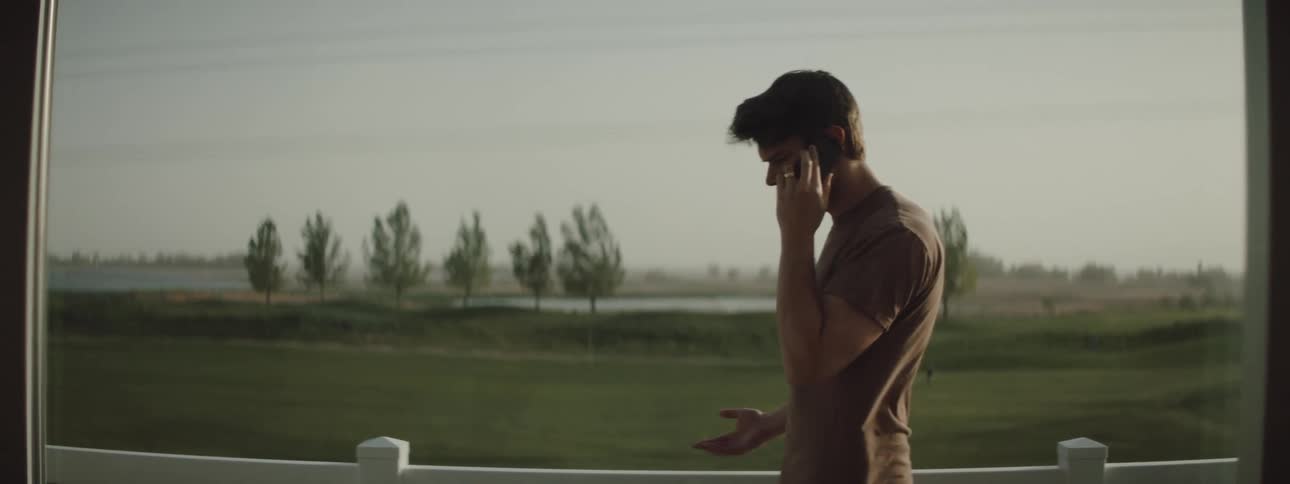 An angry male standing and walking in circles outside in the wind talking on a cell phone