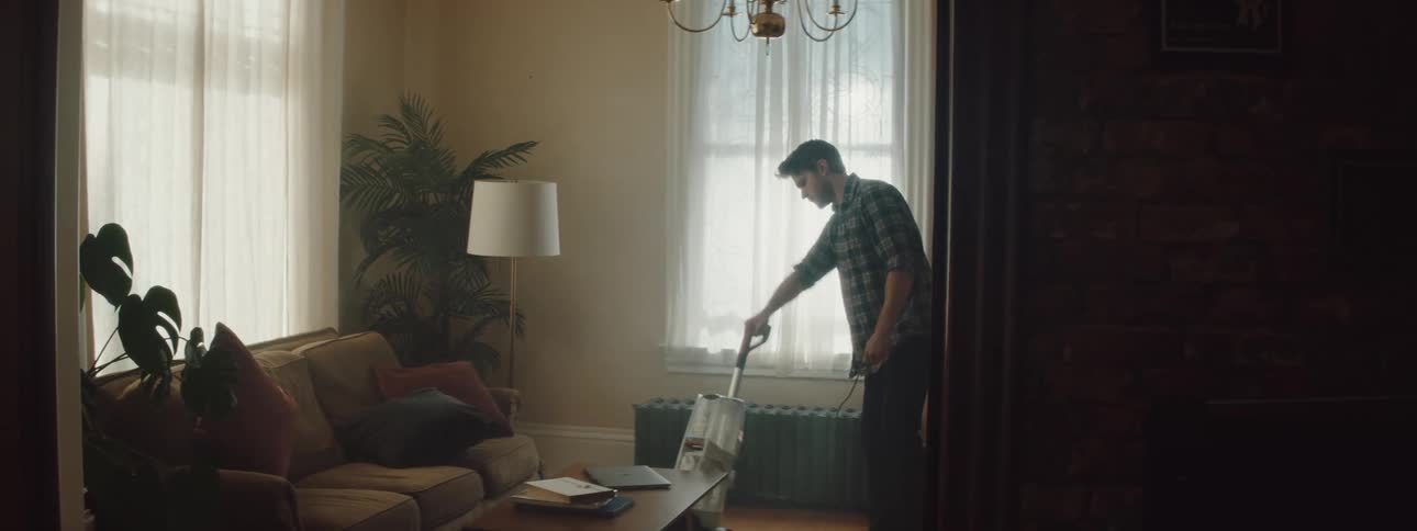 A man is vacuuming his living room during the day
