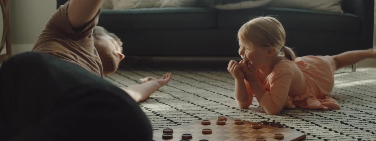 A man and child play checkers on the living room floor