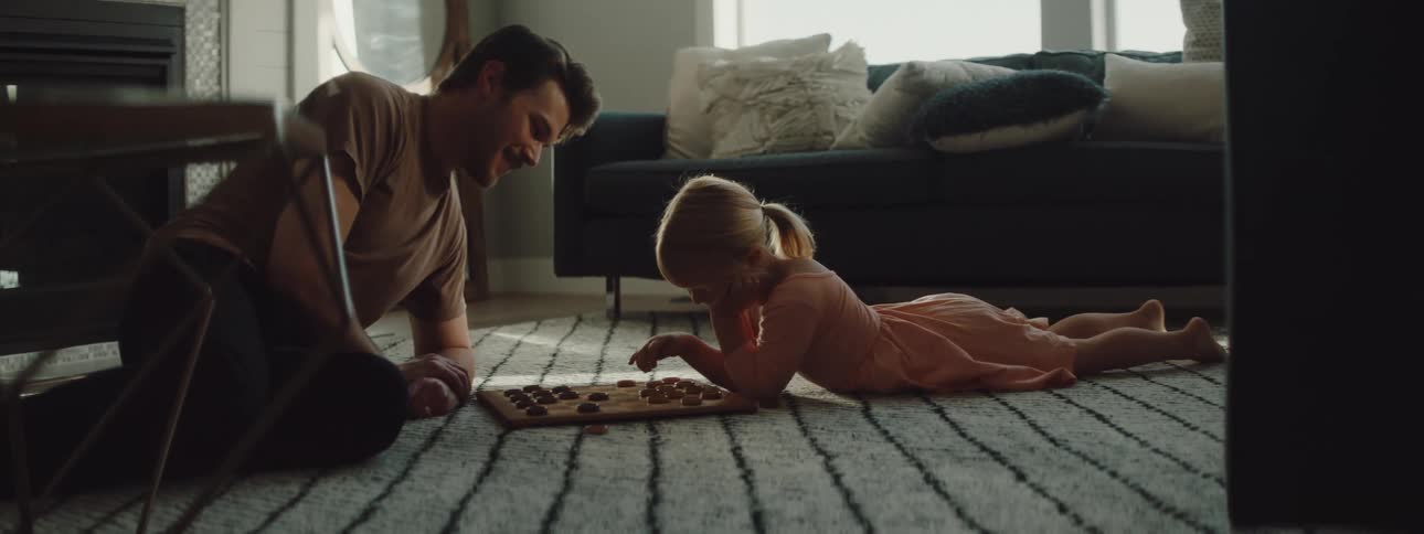 Father and daughter play checkers on while lying on living room rug
