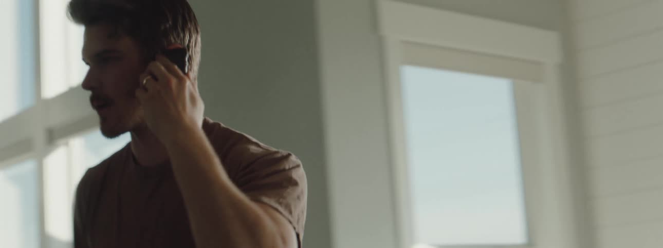 A man at home talks on his cell phone as he frantically looks around the room