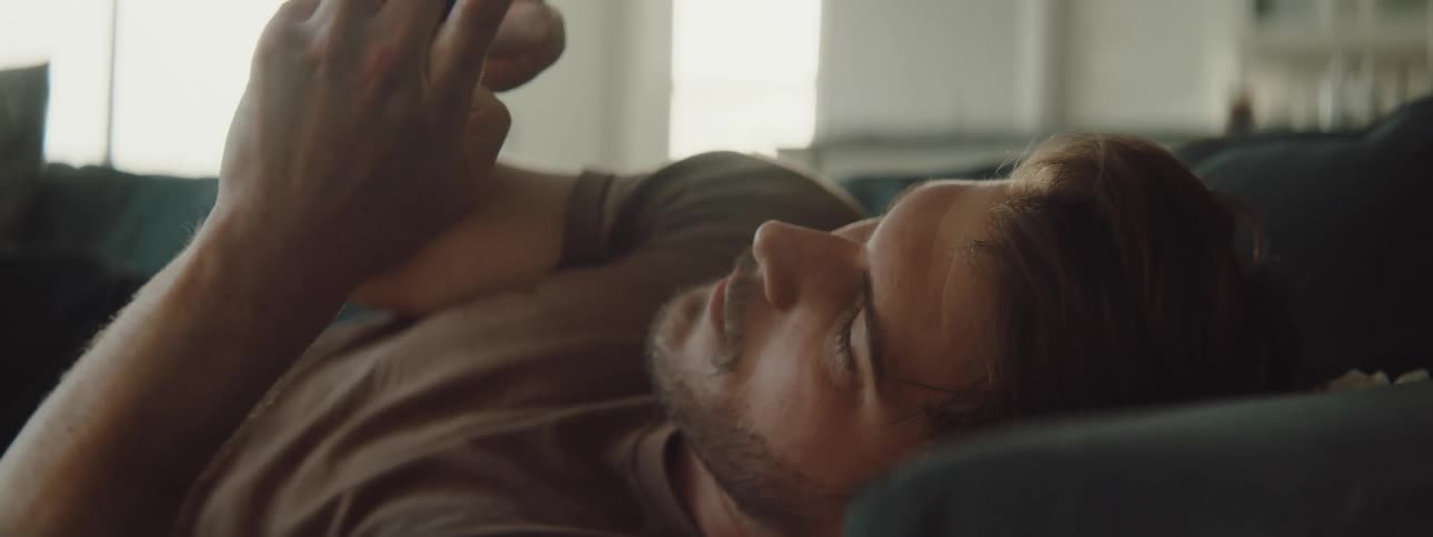 Man reclined on a couch texting on the phone at home