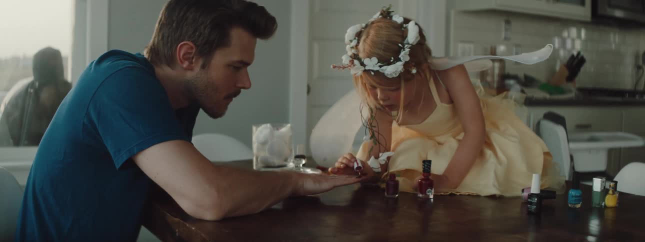 A girl in a room on a table putting nail polish on a mans nails