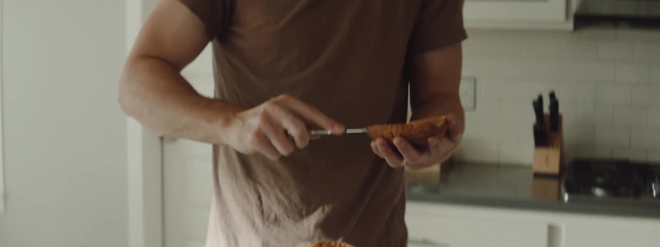 Man spreading jam on a toast while talking on the phone in the kitchen at home