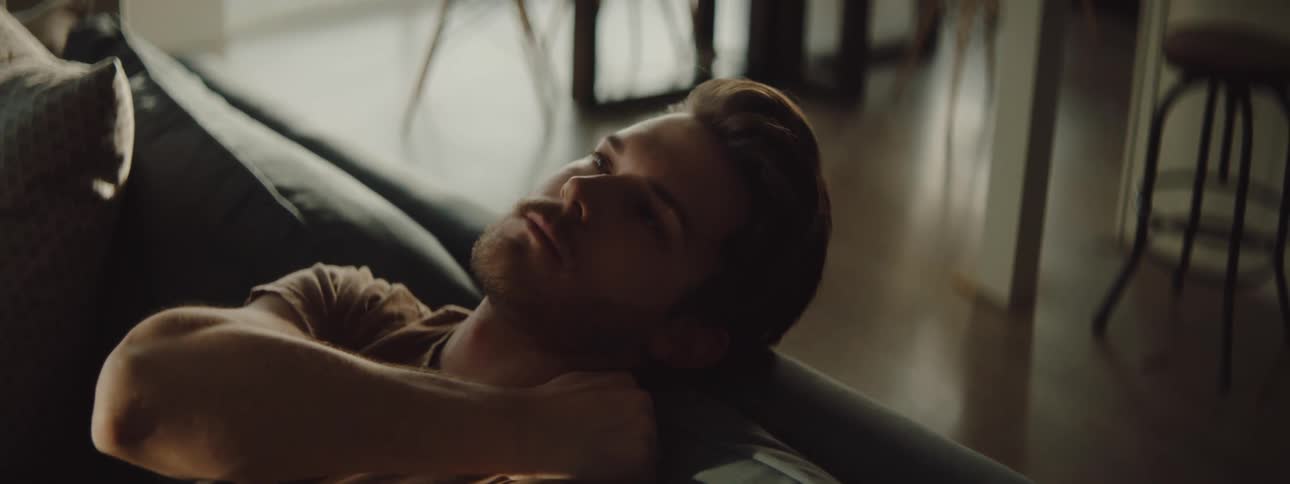 A man is sitting on his couch indoors at midday
