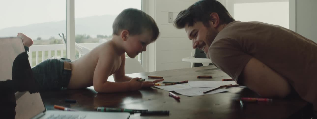 Father is talking to his son while they sit at a table next to a window