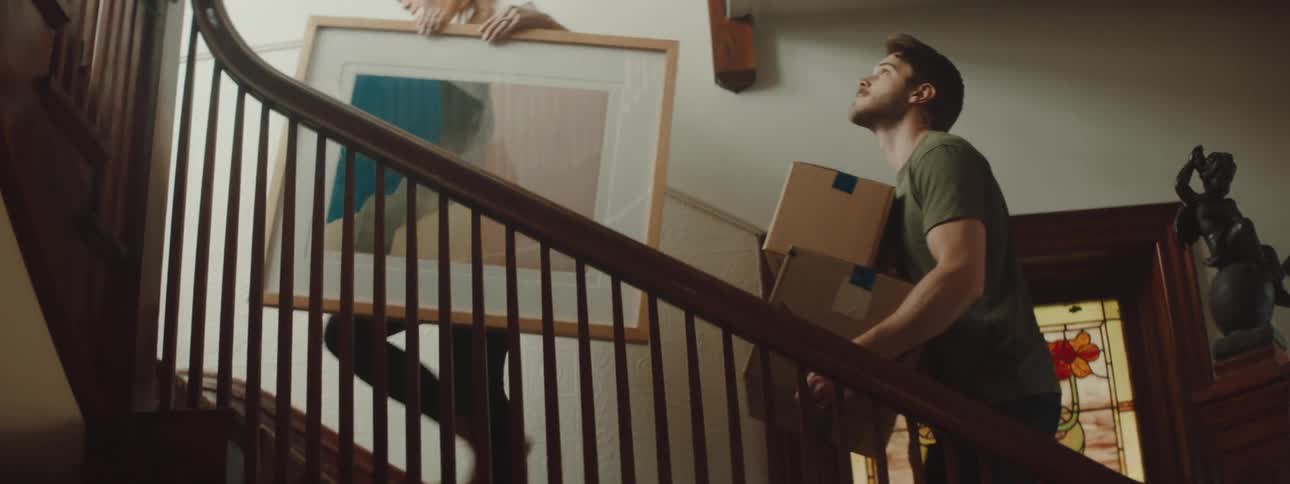 Young couple carrying boxes and a framed picture upstairs