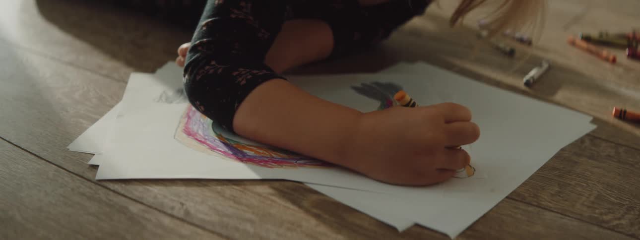 Blonde girl lying on wooden floor draws and colors with crayons