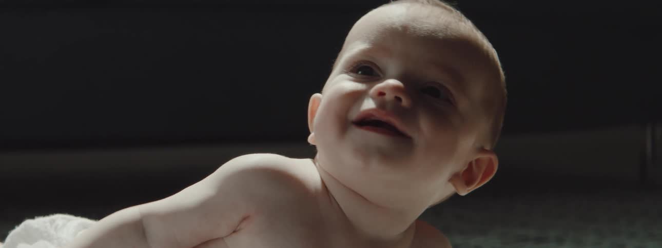 A baby lying on a rug laughs as he rolls over
