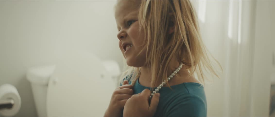 A small female child ripping off a necklace in anger in a bathroom