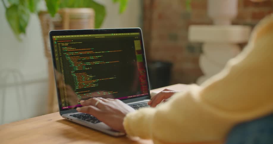 Woman wearing sweater leans over wooden table typing on laptop