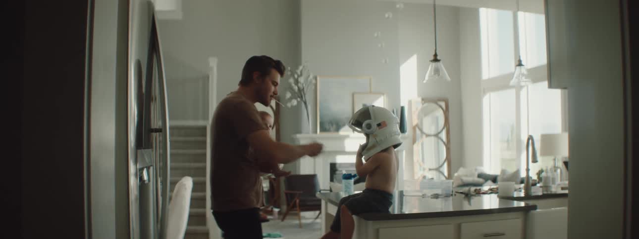 Boy wearing an astronaut helmet sitting in the kitchen countertop playing with his dad