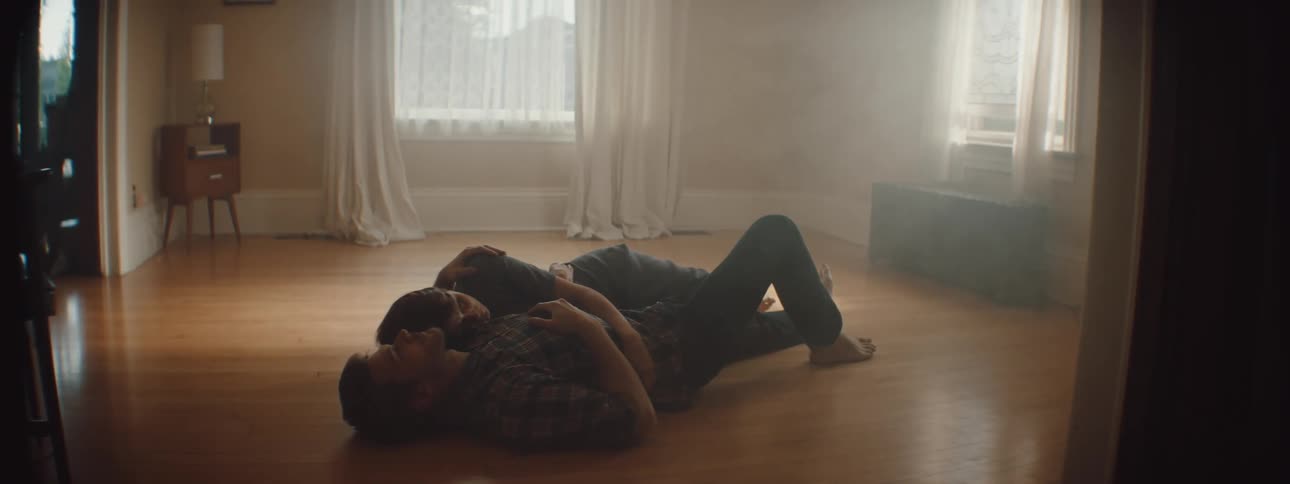 Man and woman holding each other lies on the floor in an empty room