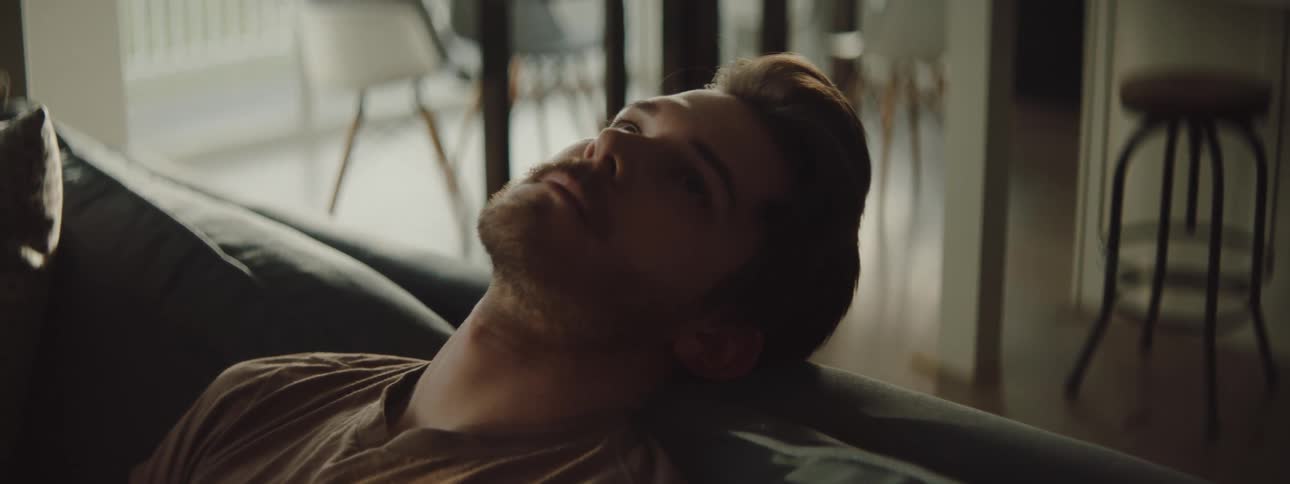 Bearded young man reclined on a couch in a dimly lit living room