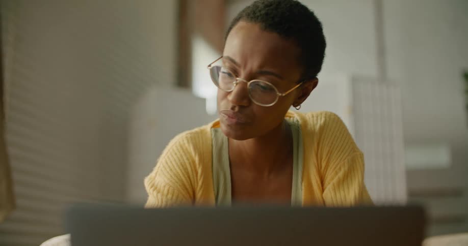 A black female sitting down at a laptop looking around and at the screen