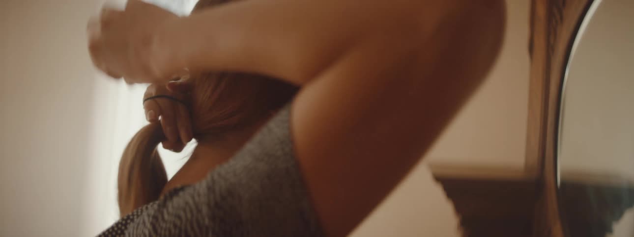 A woman is looking at a mirror and putting her hair up