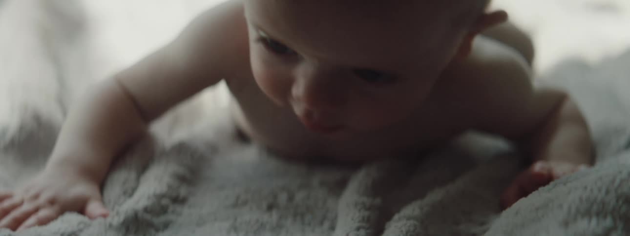 A baby with diapers in a room crawling on a blanket