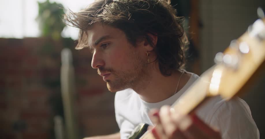 A man is sitting indoors and playing guitar
