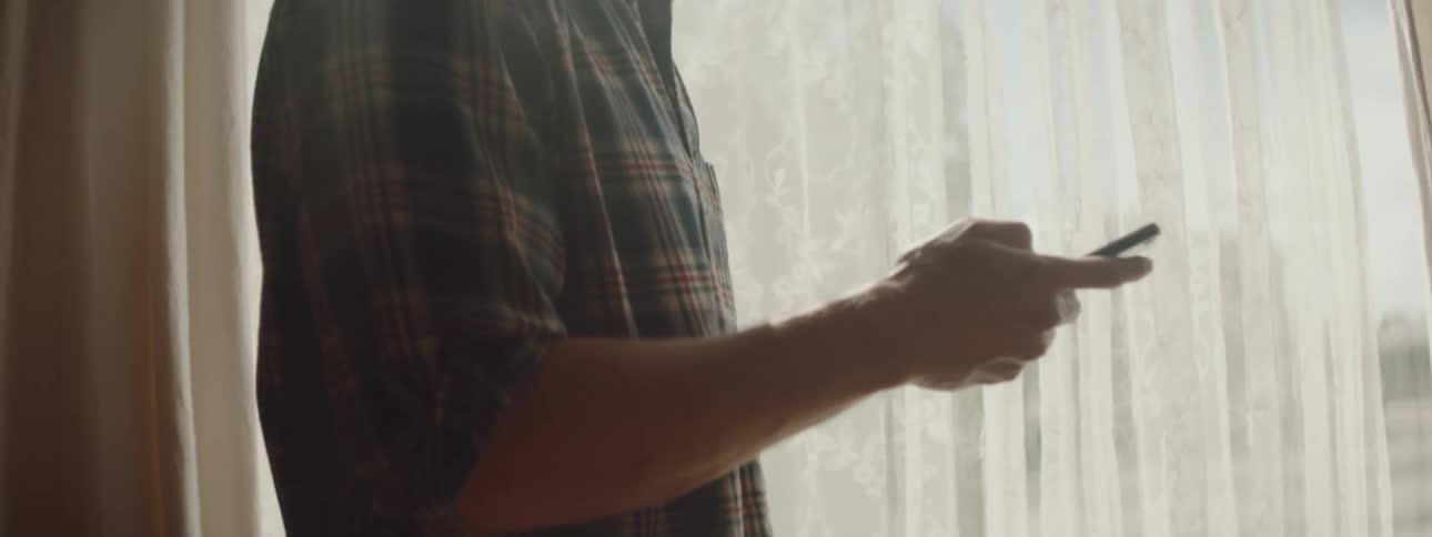 A man is walking around his house and looking at his cellphone