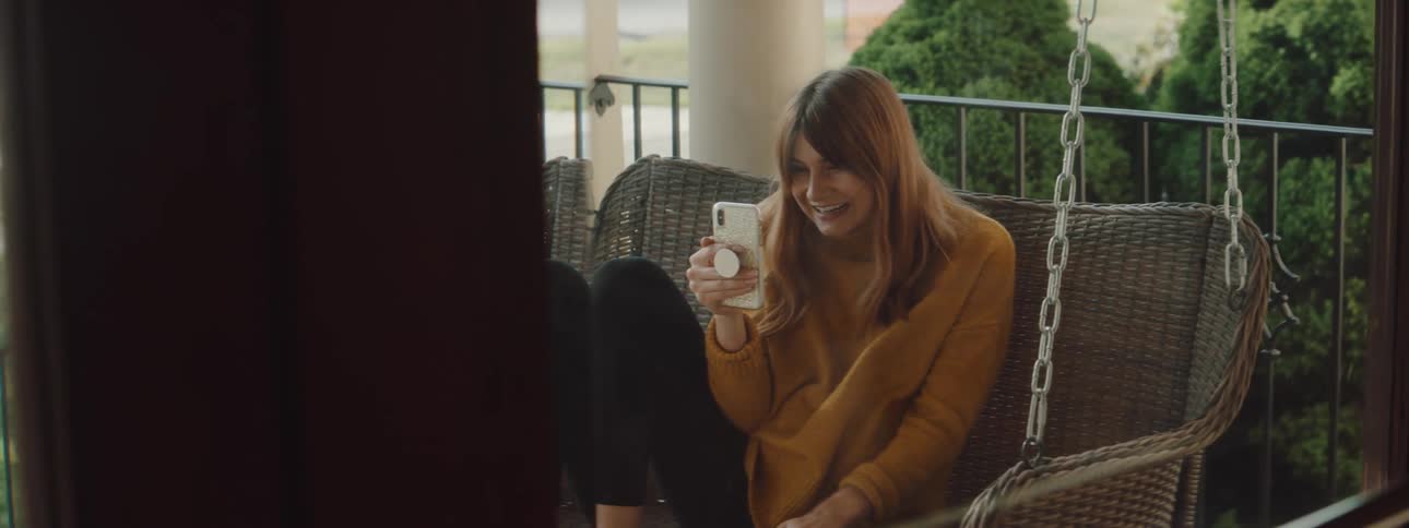 Woman sits on a porch swing while on a video chat on her cellphone
