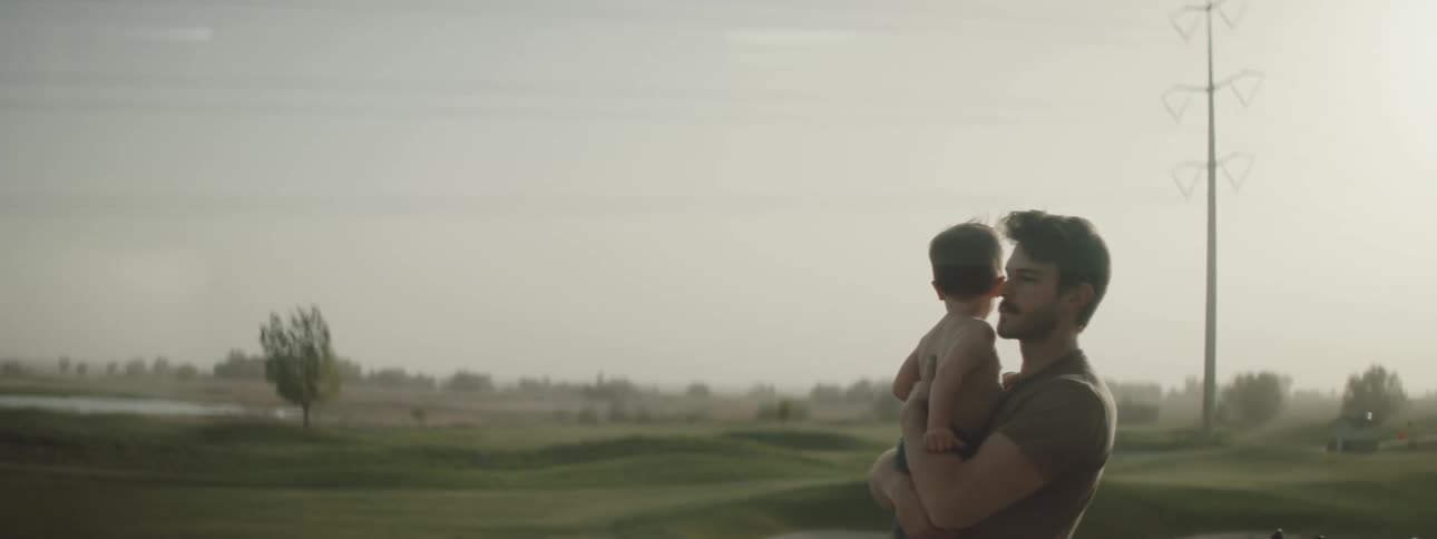 A man picking up a boy with trees the sky and clouds in the background