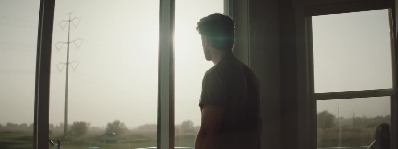 A man is standing indoors and looking out the window at the horizon