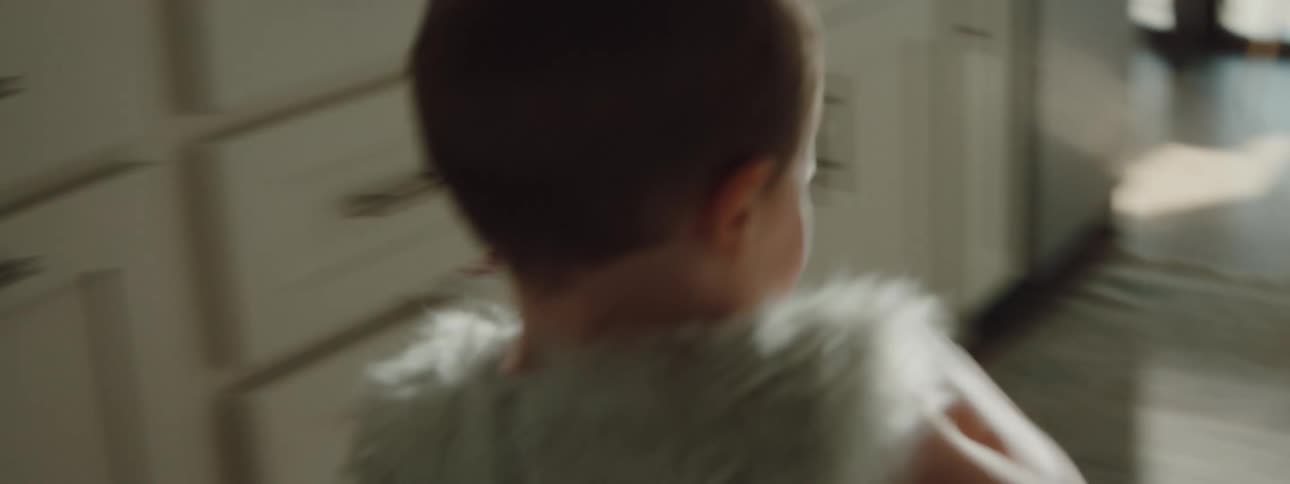 A toddler laughs running through the kitchen and crashes into sister