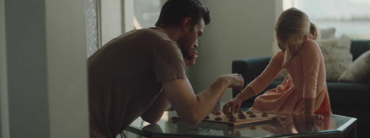 A man and a young girl are playing checkers while sitting at a coffee table