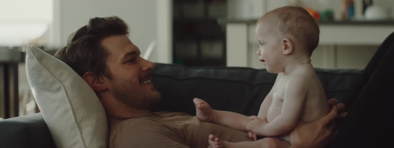 A man lays on the couch with a baby and smile