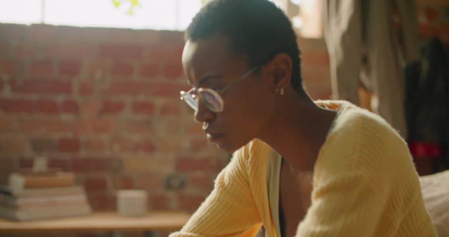A woman sitting on a home couch types on a laptop sitting on the coffee table in front of her