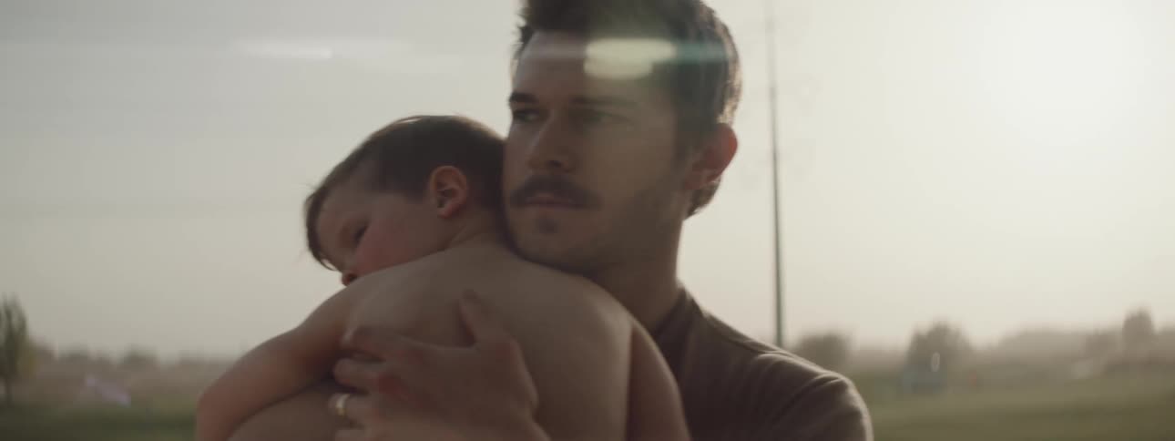 Father stands outdoors holding son stroking his back