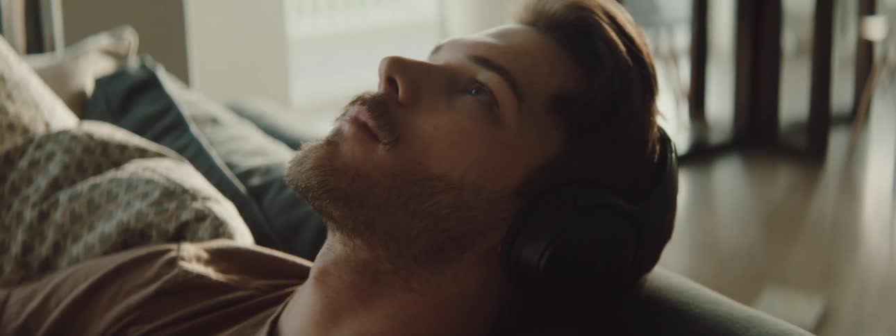 A man sitting on a couch with headphones with chairs and a table in the background