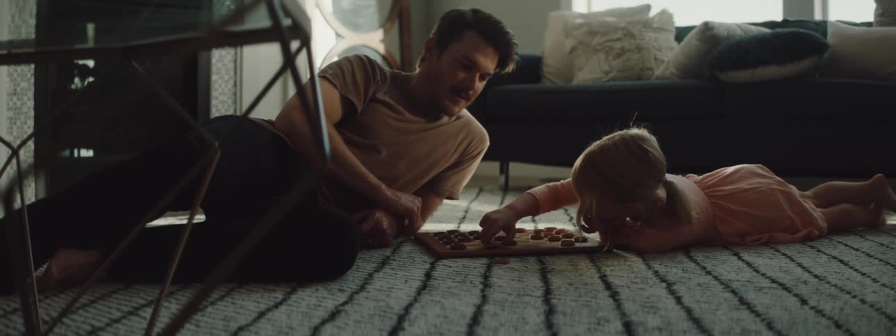A man and a girl in a room laying on the floor playing checkers