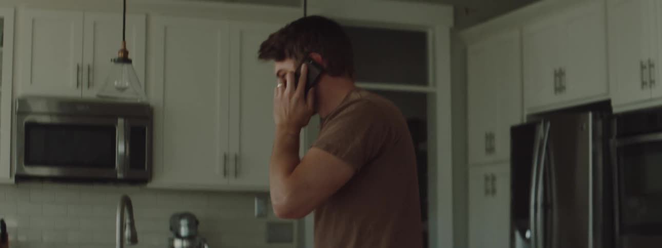 Man talking on the phone picks up his daughter dressed on a green dinosaur costume at home