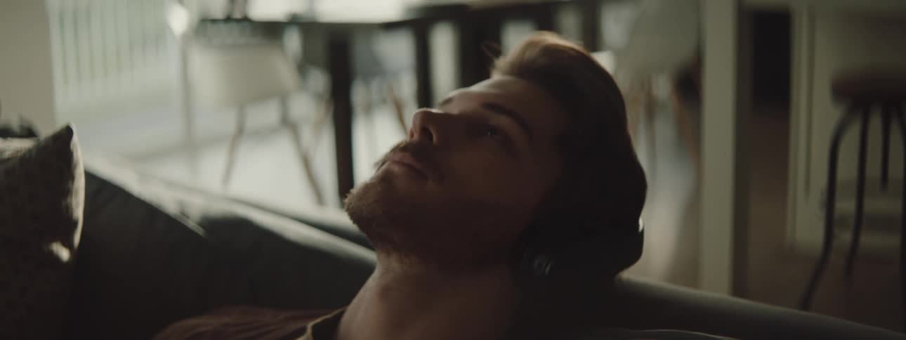 A male sitting on a couch listening to headphones and resting his head