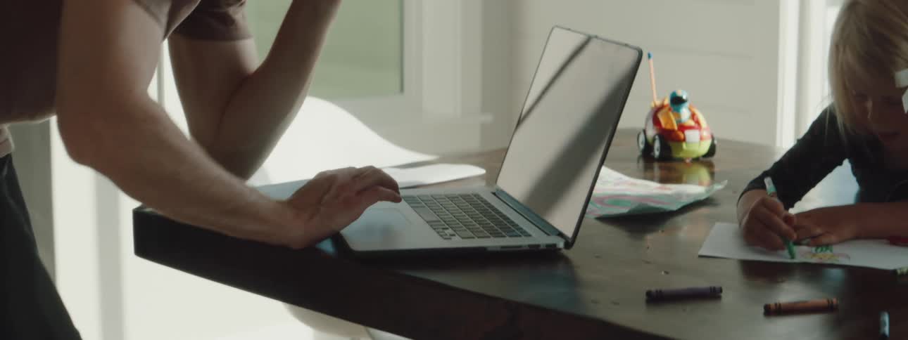 A father is on his cell phone and looking at a laptop