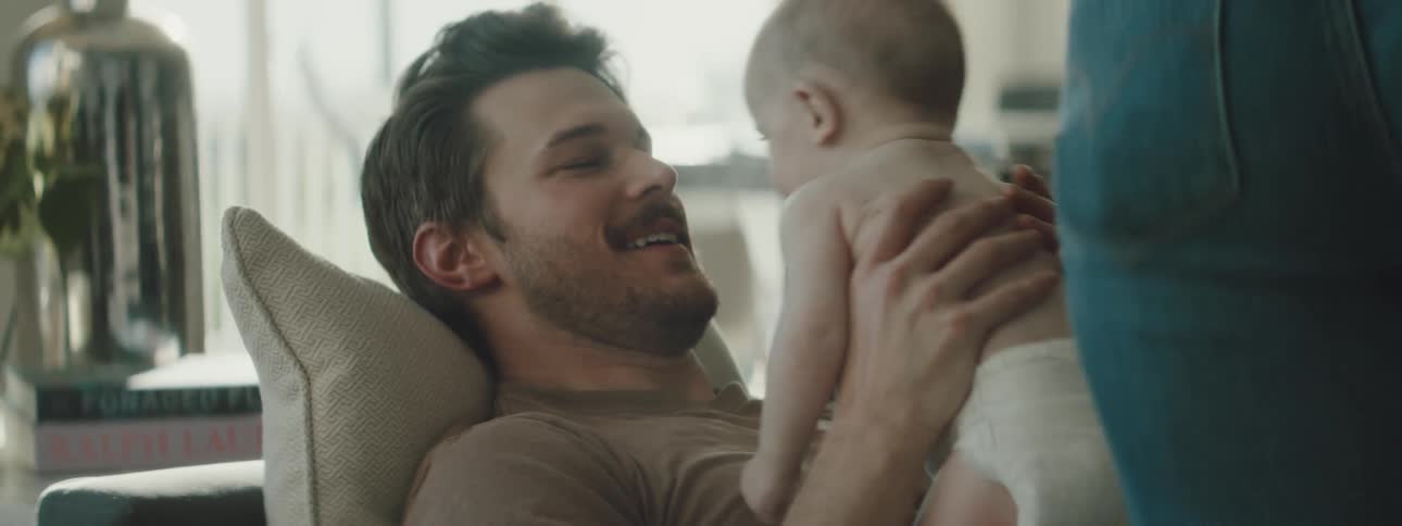 A father is laying on the couch and holding his baby