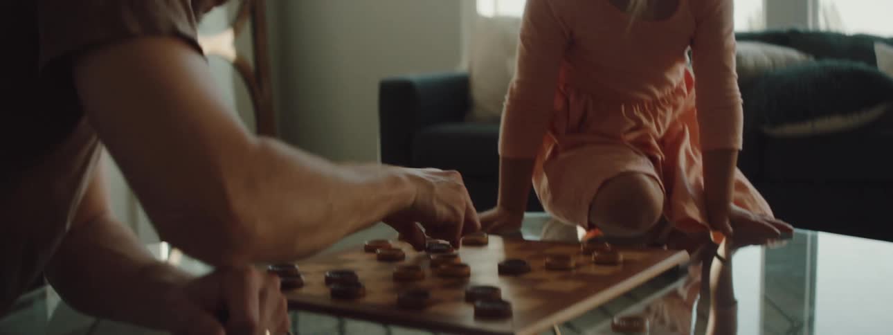 Father and daughter play checkers on glass table